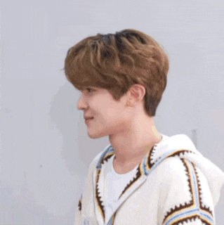 a young man wearing a white sweater with a hood is standing in front of a wall .
