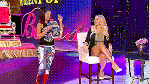 a woman is standing next to a woman sitting in a chair holding a microphone .