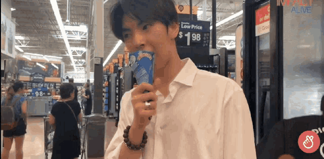 a man in a white shirt drinks from a can in a store with a sign that says low price