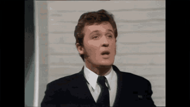 a man in a suit and tie is making a funny face while standing in front of a brick wall .