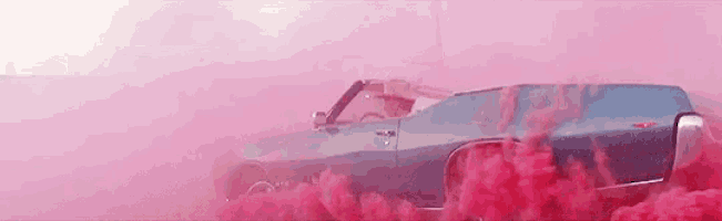 a blue car is driving through a pink cloud of smoke .