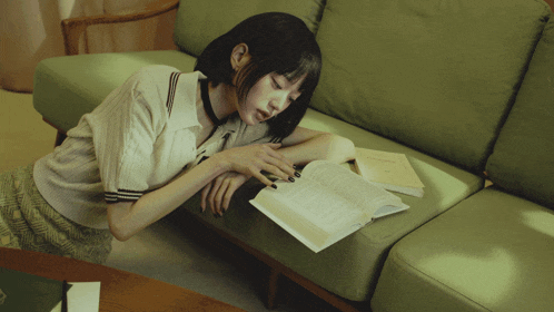a woman is laying on a green couch reading