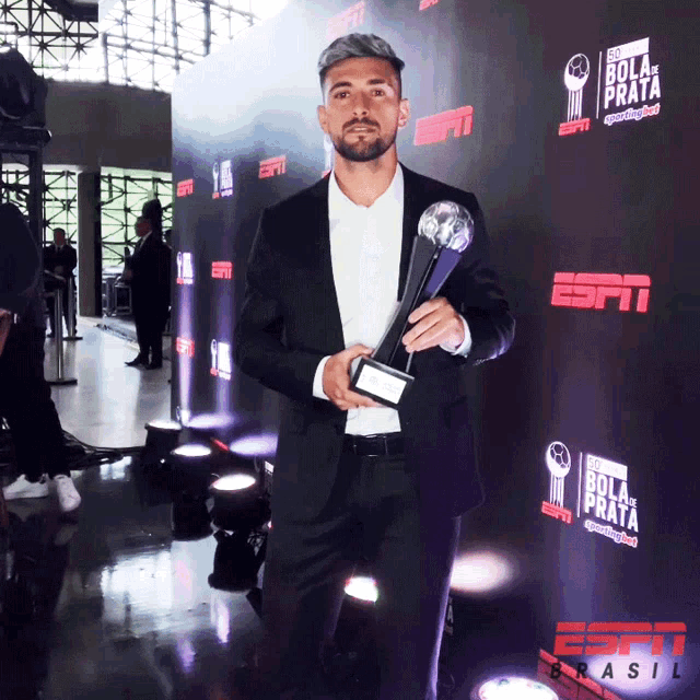 a man in a suit is holding a trophy in front of a wall that says espn brasil