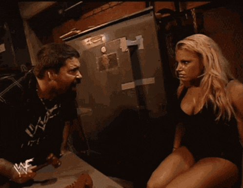 a woman in a black tank top is standing next to a man in a wrestling uniform