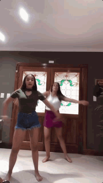 two girls are dancing in front of a door with a stained glass window