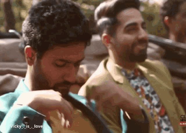 a man in a green suit and tie is sitting next to another man
