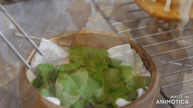 a wooden bowl filled with green leaves is being made by animatica