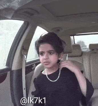 a young girl wearing a black shirt and a pearl necklace is sitting in the back seat of a car ..