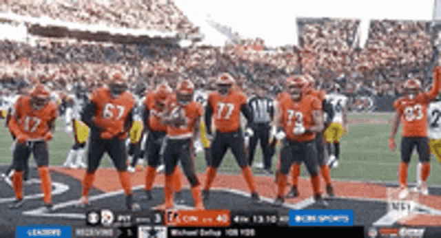 a group of football players in orange uniforms are standing on the field .