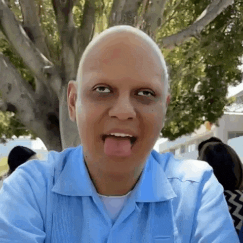 a bald man in a blue shirt is sticking his tongue out while making a funny face .