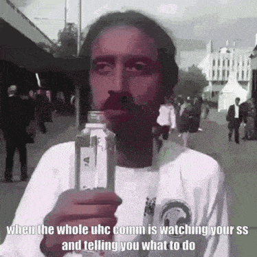 a man with a mustache is holding a bottle of water and talking to someone .