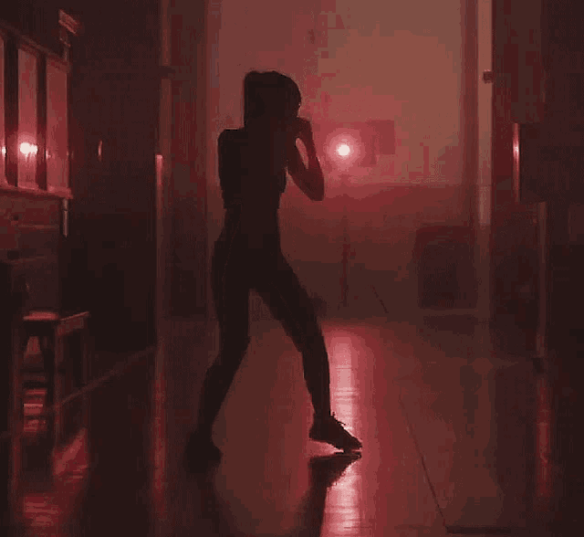 a silhouette of a woman dancing in a hallway with a red light behind her