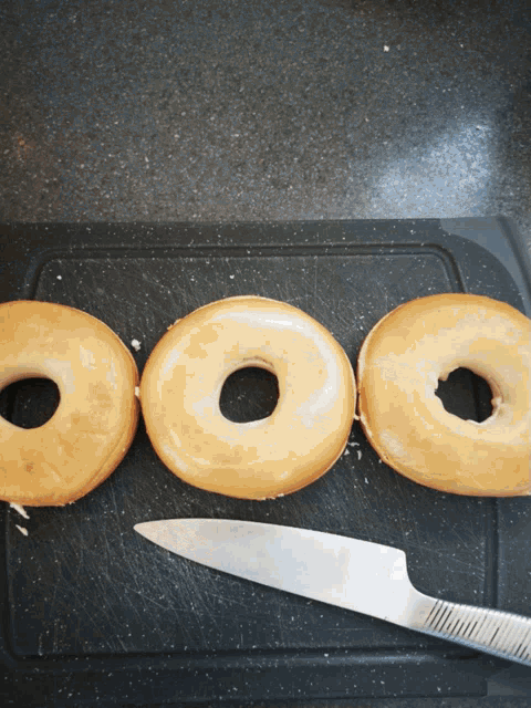 three donuts on a cutting board with a knife next to them
