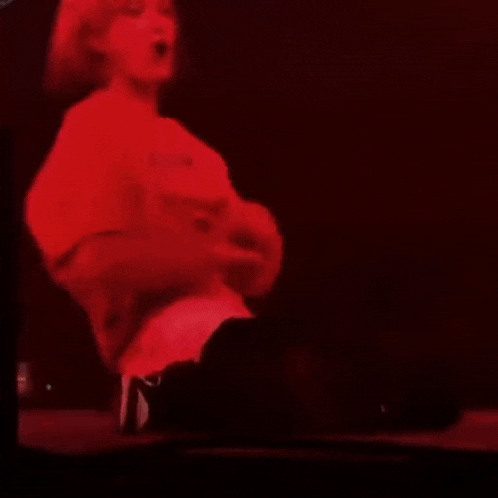 a man in a red shirt is sitting on the floor on a stage in front of a microphone .