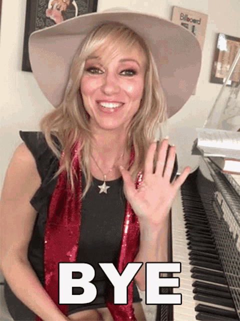 a woman wearing a hat and a scarf is sitting at a piano and waving her hand with the words bye below her