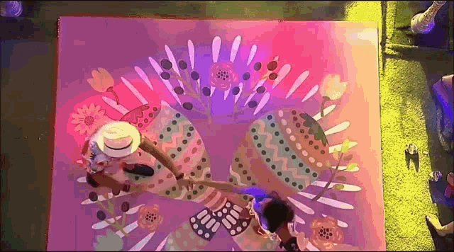 a woman in a white hat is painting a circle of flowers on a pink surface