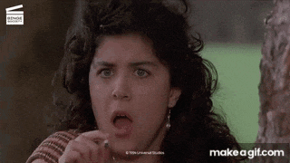a woman with curly hair is making a funny face while standing next to a tree .