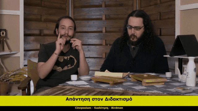 two men are sitting at a table with a sign that says cineposium on it