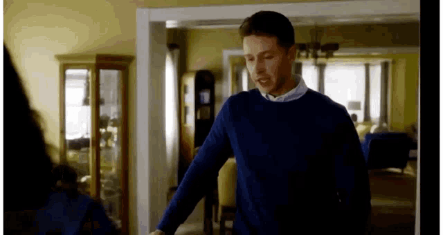 a man in a blue sweater is standing in a living room looking at a woman .