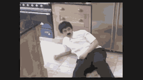a man with a mustache is laying on the floor of a kitchen