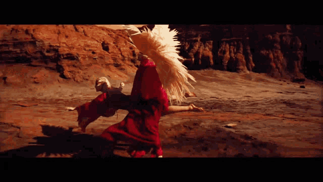 a woman in a red dress with white feathers on her head is dancing in the desert