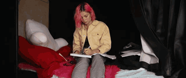a woman with pink hair is writing in a notebook