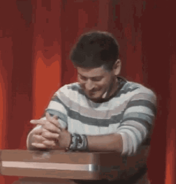a man is sitting at a table with his hands folded .