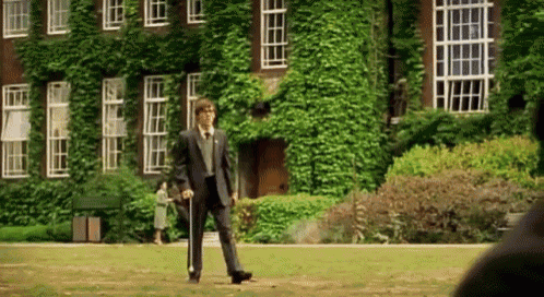 a man in a suit and tie is walking in front of a building with ivy on it