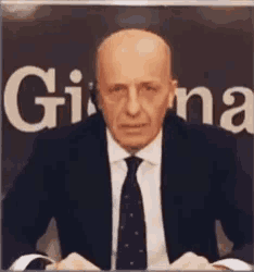 a man in a suit and tie is sitting in front of a sign that says gina on it
