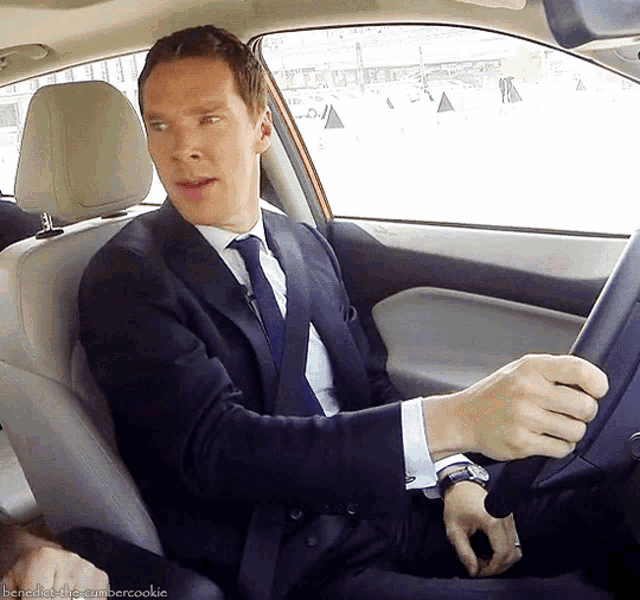 a man in a suit and tie driving a car