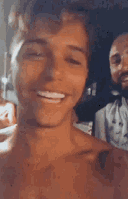 a shirtless man is smiling while standing next to another man .