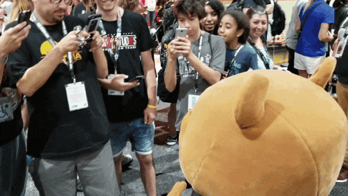 a group of people standing around a stuffed animal wearing a black shirt that says studios on it
