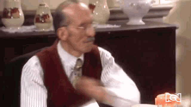 a man in a red vest and tie is sitting at a table with a candle on it