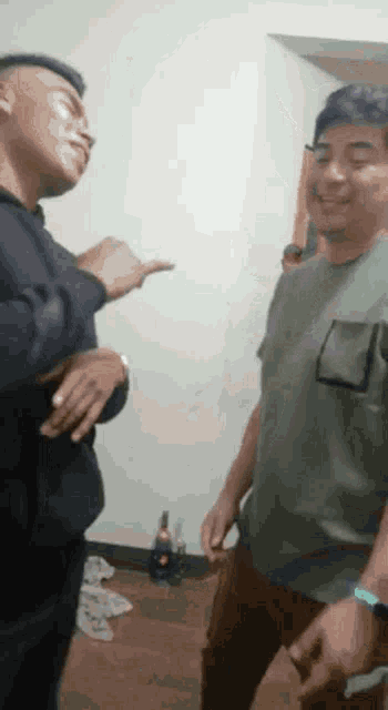 two men are standing next to each other in a room . one of the men is wearing a green shirt .