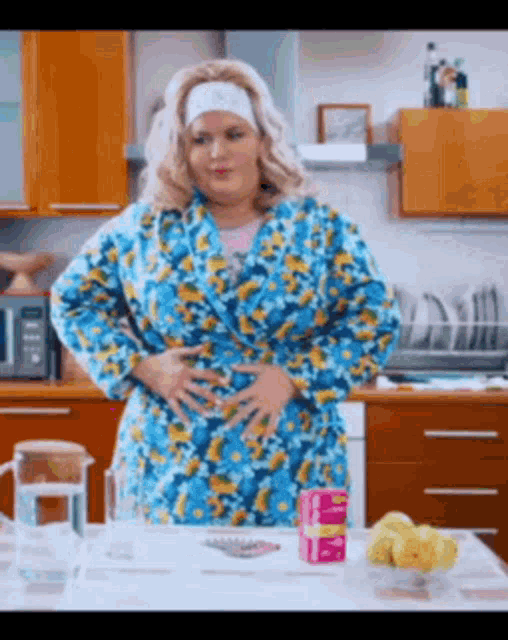 a woman in a blue robe is standing in a kitchen holding her belly .