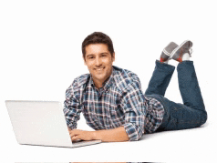 a man in a plaid shirt is laying on the floor using a laptop