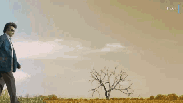 a man in a suit walks through a grassy field with a sivaji logo in the background