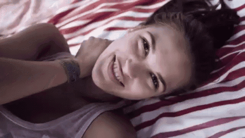 a woman is laying on a striped blanket on a bed and smiling .