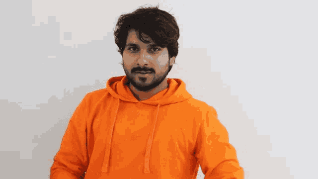 a man wearing an orange hoodie making a heart shape with his hands