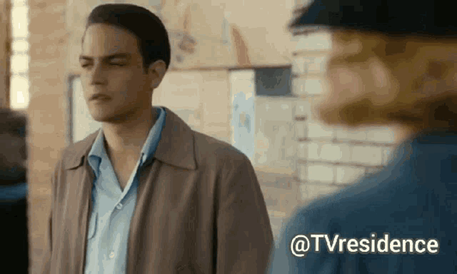 a man in a brown jacket is standing next to a woman in a blue shirt and the words @tvresidence are above him
