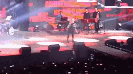 a woman is singing into a microphone on a stage with a band behind her