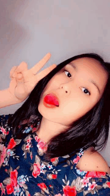 the girl is wearing a floral shirt and making a peace sign .