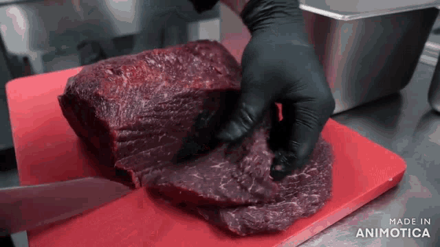 a person is cutting a large piece of meat on a red cutting board that says made in animatica