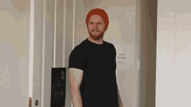 a man wearing a red hat and a black shirt stands in front of a sign that says toilets this way