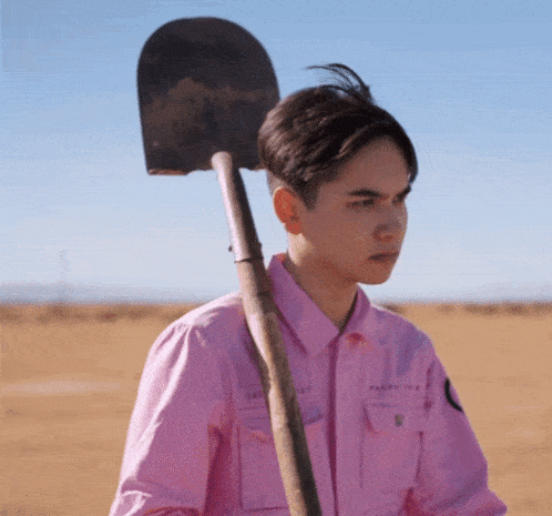 a young man in a pink shirt is holding a shovel over his shoulder
