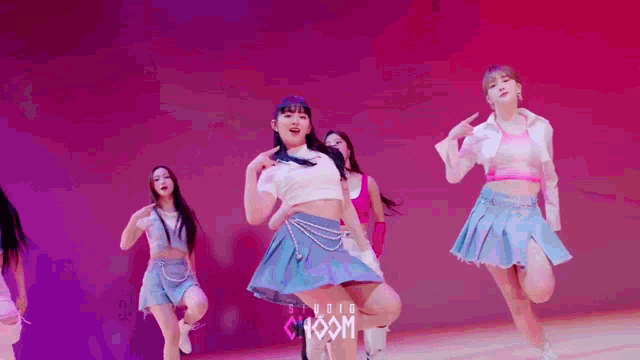 a group of young women are dancing on a stage in front of a pink background .