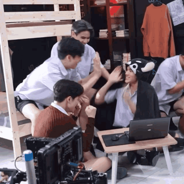 a group of young men are sitting around a small table with a laptop
