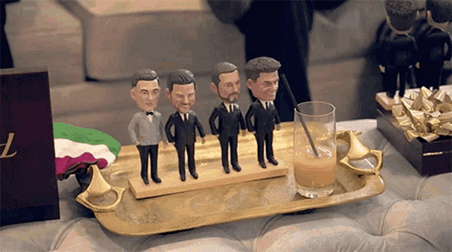 a tray with a glass of orange juice and four figurines of men on it