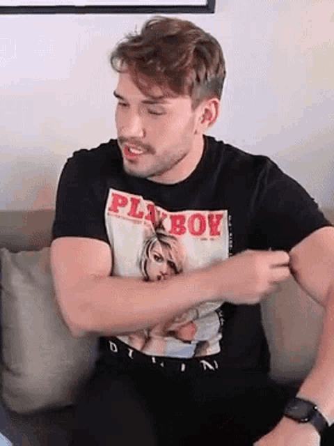 a man wearing a black playboy shirt is sitting on a couch .