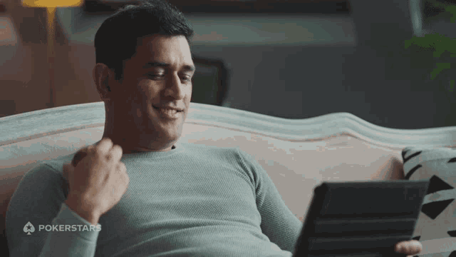 a man sitting on a couch looking at a tablet with a pokerstars logo on the bottom